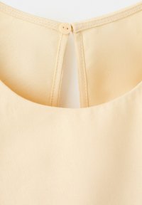 Țesătură de culoare crem cu o mică nasture rotundă la spatele gâtului unei haine.