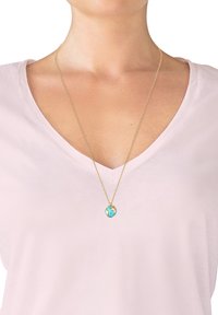 Gouden ketting met een turquoise wereldbol hanger, gedetailleerd met gouden accenten, gedragen over een lichtroze V-hals shirt.