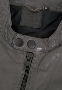 Innenansicht einer grauen Lederjacke mit Reißverschluss und zwei schwarzen Druckknöpfen am Kragen. Größe M. Weiches, strukturiertes Material.