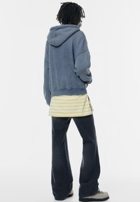 Hoodie aus einer Baumwollmischung in verblasstem Blau, kombiniert mit einem gelb-weiß gestreiften Lagenhemd und dunklen ausgestellt geschnittenen Jeans. Lässiges Design, entspannte Passform.