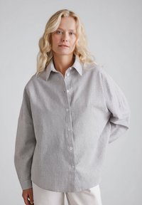 Szara i biała koszula w kratę na guziki z klasycznym kołnierzykiem, luźnym krojem i długimi rękawami, wykonana z lekkiego materiału.