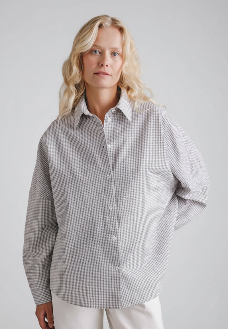 Szara i biała koszula w kratę na guziki z klasycznym kołnierzykiem, luźnym krojem i długimi rękawami, wykonana z lekkiego materiału.
