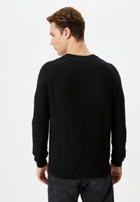 Czarny sweter dzianinowy z ribbowaną fakturą, długimi rękawami, okrągłym dekoltem i dopasowanym dołem. Tylny widok podkreśla design raglanowych rękawów.