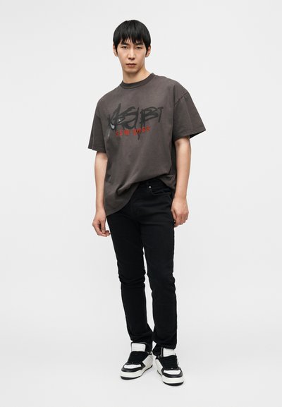 Γραφικό μπλουζάκι σε σκούρο γκρι βαμβάκι με μαύρο και κόκκινο κείμενο. Στενά μαύρα τζιν και ασπρόμαυρα αθλητικά παπούτσια ολοκληρώνουν το σύνολο.