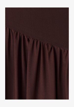 Tela marrón oscuro con textura de malla fina recogida en diagonal a lo largo de la parte inferior, creando pliegues y dobleces suaves.