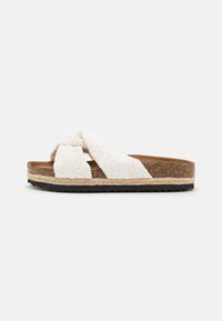 Sandales blanches à glissière avec un dessus en tissu texturé, un design à brides croisées, une semelle intermédiaire en liège et une semelle extérieure en caoutchouc noir.
