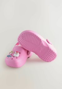Roze klompen gemaakt van duurzaam materiaal met ventilatiegaten, voorzien van decoratieve 3D-charms van een rendier en een sneeuwfiguur. Getextureerde zool.