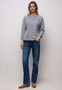 Grijs-wit gestreept shirt met lange mouwen en een ronde hals, gecombineerd met middelblauwe jeans met rechte pijpen en lichtbruine enkellaarsjes.