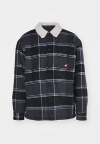 Schwarze und graue karierte Jacke mit einem mit Fell gefütterten Kragen, ausgestattet mit Knöpfen und einer Brusttasche mit einem Logo-Patch. Weicher Stoff.