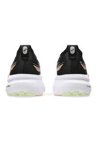 Zwarte sportschoenen met een gestructureerde bovenkant, witte tussenzool en lichtgroene buitenzool. Beschikt over een logo op de achterkant en metallic accenten.
