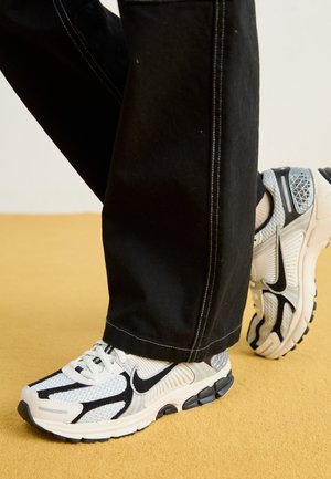 Baskets Nike avec un schéma de couleurs noir, blanc et gris. Comportant des panneaux en maille et solides, des semelles en caoutchouc épaisses et un détail de talon surélevé.