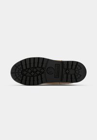 Black rubber outsole with deep treads and Timberland logo. Upper is tan leather with stitching details. Flat design for stability and grip.