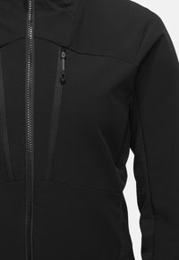 Schwarze Softshell-Jacke mit einem Reißverschluss vorne, strukturierten Stoffakzenten und einer taillierten Passform. Enthält zwei vertikale Reißverschlusstaschen.