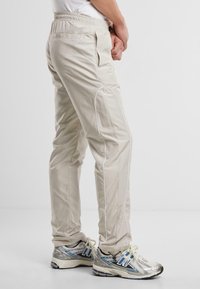 Beige lichte broek met elastische tailleband, zijzakken en witte piping langs de naden. Gekocht met zilveren hardloopschoenen.