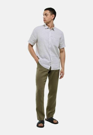 Chemise en lin gris clair à manches courtes avec une poche, associée à un pantalon vert olive et des sandales noires à enfiler, créant une tenue décontractée.
