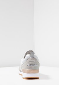 Gray and white sneaker with a smooth and textured finish, featuring a padded collar, pull tab, and rubber sole. "SKECHERS" logo visible.