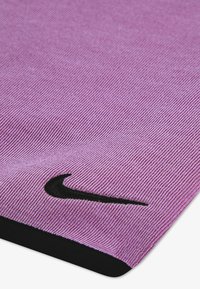 Μωβ ύφασμα με διαγώνια ραβδωτή υφή, που διαθέτει μαύρο λογότυπο Nike στο κάτω αριστερό μέρος και αντίθετο μαύρο περίγραμμα.