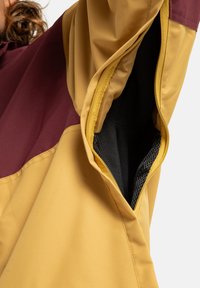 Jacke mit Farbblockdesign in Gelb und Bordeaux, mit einer zipbaren Tasche und glatter Textur. Sichtbares Innenfutter aus Netz.