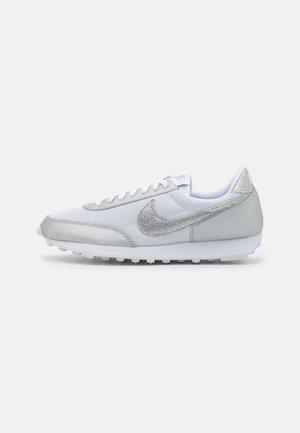 Baskets Nike blanches et argentées avec détails en mesh et daim, fermeture à lacets et semelle texturée, vues de côté sur fond uni.