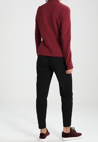 Bordowy sweter z dzianiny w białe kropki, zestawiony z czarnymi tapered spodniami i ciemnorudymi sneakersami. Prosty design, długie rękawy i dopasowany krój.