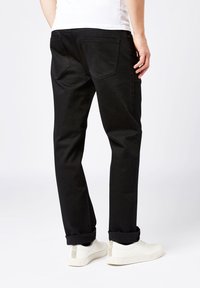 Jeans negros de corte slim, diseño de cinco bolsillos y costuras visibles. Combinados con zapatillas blancas que tienen un detalle texturizado en la parte trasera.