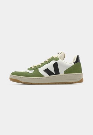 Zapatillas de ante verde y cuero blanco con acentos negros, puntera perforada y suela de goma beige, con un logo visible en el lateral.