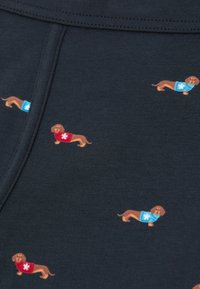 Una tela azul marino presenta pequeños dachshunds de estilo caricaturesco con suéteres rojos y azules, cada uno decorado con un patrón de copos de nieve blancos.