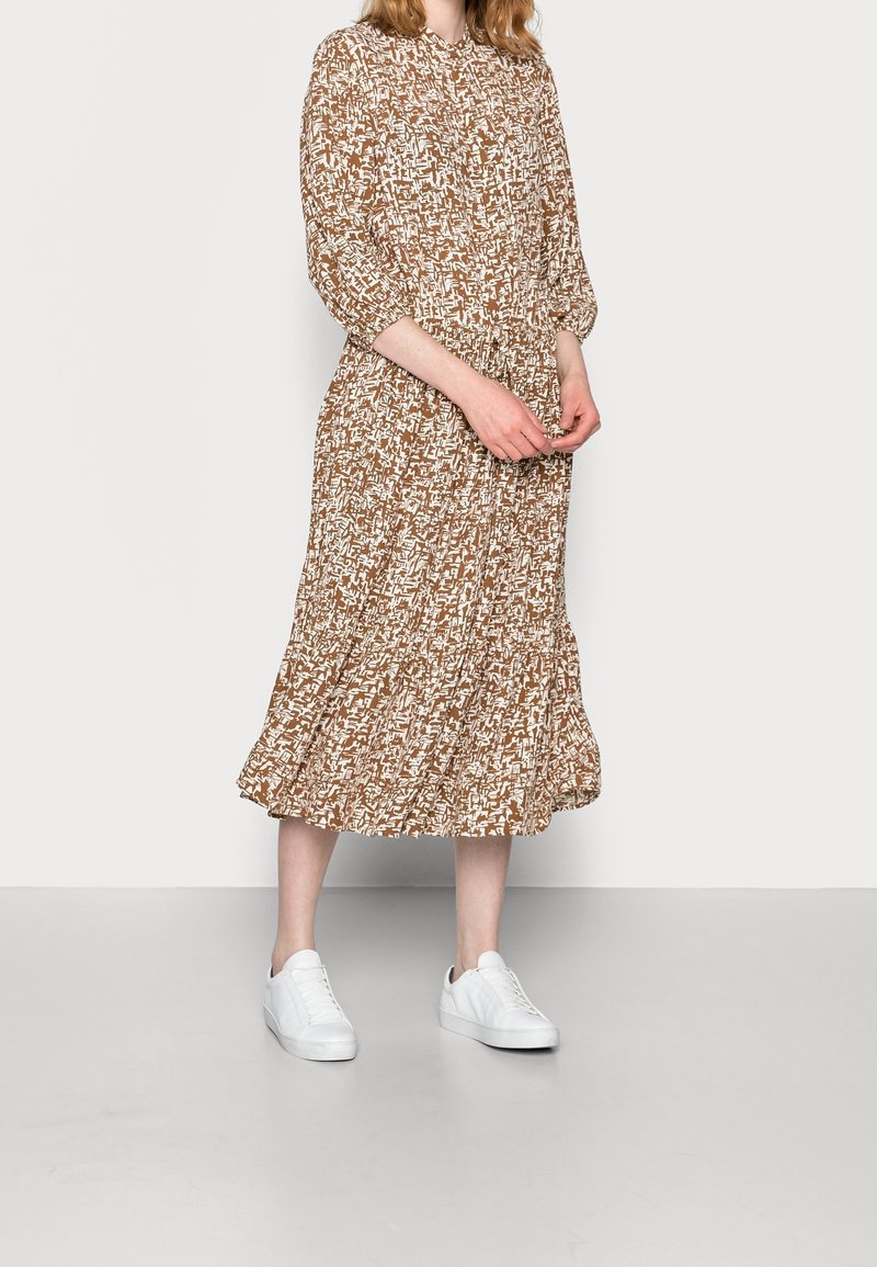 Abito midi marrone con motivo astratto bianco, scollatura rotonda, maniche a tre quarti e orlo arricciato, abbinato a sneakers bianche.