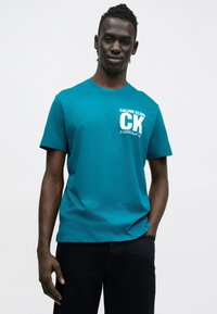 Azúrové bavlnené tričko s krátkymi rukávmi, okrúhlym výstrihom, s nápisom "CALVIN KLEIN" a logom "CK" v bielej farbe na ľavej strane. Jednofarebné, ležérny strih.