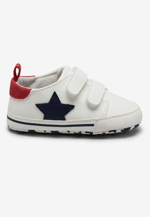 White toddler sneakers with navy star detail, red heel tab, Velcro straps, and a rubber sole featuring a striped pattern.