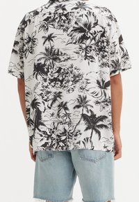 Camicia a maniche corte con motivo floreale bianco e nero con palme. Tessuto leggero, vestibilità comoda, orlo curvo, abbinata a pantaloni corti di jeans.