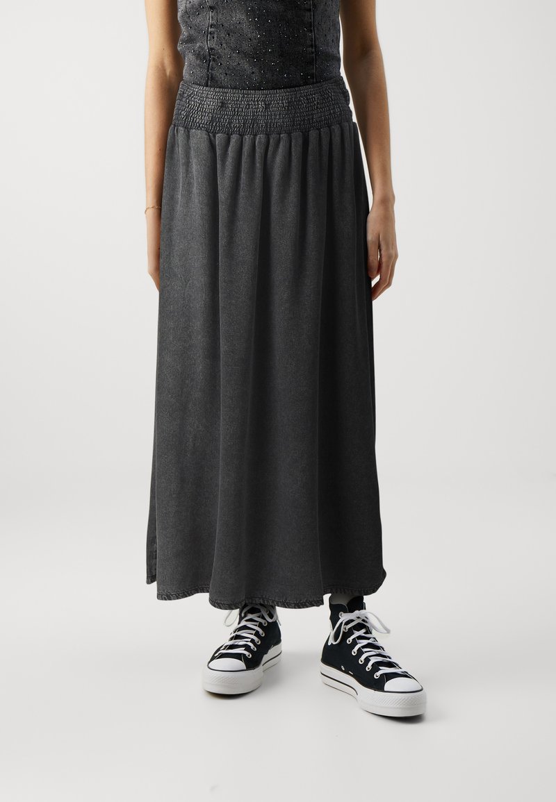 Grå maxi nederdel med elastisk talje, lavet af blødt stof, med et flydende design og en kant med en subtil flosset detalje. Sammen med sorte høj-top sneakers.