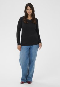 Black long-sleeve top with lace detailing on sleeves, paired with light blue wide-leg jeans. Model stands on a plain background.
