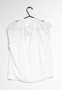 White, lightweight sleeveless top made of sheer fabric, featuring a round neckline and a smooth texture, hung on a black hanger.