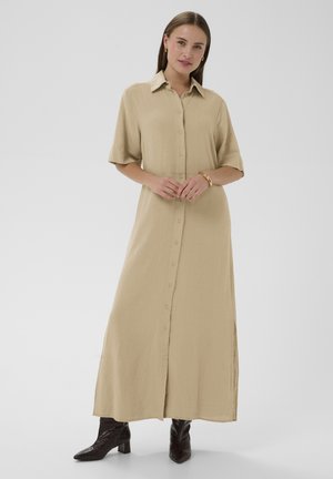 Beige maxi-jurk met knopen en korte mouwen, gemaakt van zachte stof, met een rechte snit en zijsplitsingen. Zwarte enkellaarzen met een spitse neus.