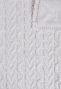 Couverture en tricot blanche avec un motif de câble texturé et une bordure lisse. Matériau doux et confortable avec un design légèrement en relief.