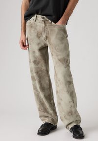 Ανοιχτό γκρι τζιν με φαρδύ παντελόνι και ξεθωριασμένο, μαρμαροειδές μοτίβο. Κατασκευασμένα από denim, με μπροστινές τσέπες, κούμπωμα με κουμπί και φερμουάρ, και χαλαρή εφαρμογή.