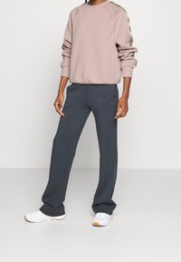Sweatshirt rose clair avec un col ras du cou côtelé et une bande latérale à motifs, associé à un pantalon de survêtement bleu marine avec des jambes fuselées et un détail de logo.