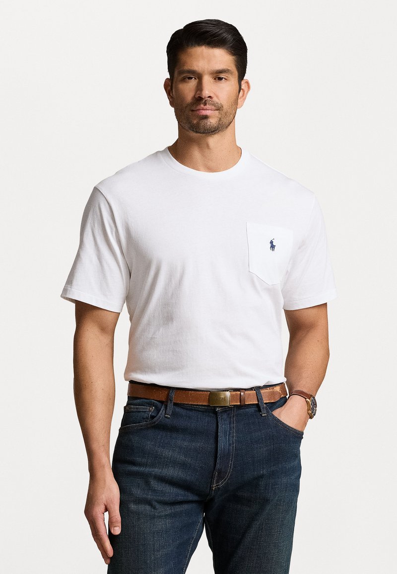 White cotton t-shirt with short sleeves, featuring a pocket on the left side and a small blue logo. Paired with dark denim jeans and a brown belt.