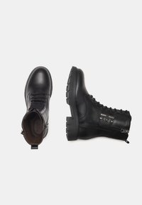 Zwarte leren enkelboots met een ronde neus, vetersluiting aan de voorkant, zijrits en een gestructureerde rubberen zool; heeft een reliëflogo-detail.