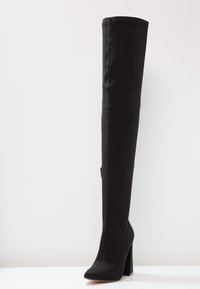 Stivale nero sopra il ginocchio realizzato in tessuto liscio, con punta appuntita e tacco a blocco testurizzato. Design senza cuciture con accenti minimi.