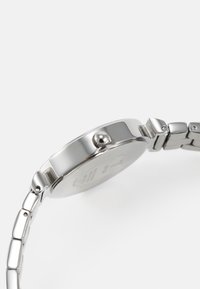 Montre-bracelet en métal argenté avec un boîtier rond, une lunette lisse et un bracelet à maillons texturés. Comprend une couronne pour régler l'heure.