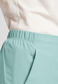 Helleblaue, elastische Bundhose aus weichem Stoff mit glatter Textur, mit seitlichen Falten und einem lässigen Schnitt.