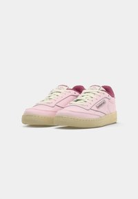 Roze tenisice s glatkom kožnom gornjom površinom, jastučićem na jeziku i ovratniku, bijelim vezicama i bež gumiranim potplatom. Sadrži Reebok logo.