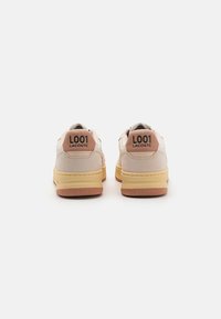 Lacoste L001 sportbačiai šviesiai kremine spalva su rožiniais akcentais, su guminėmis padais ir juodu logotipu ant nugaros. Textūruotos paviršiai.