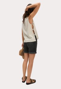 Top de tirantes con rayas claras y atados laterales, combinado con pantalones cortos negros y sandalias planas. Sosteniendo un sombrero de paja, visto desde la parte posterior.