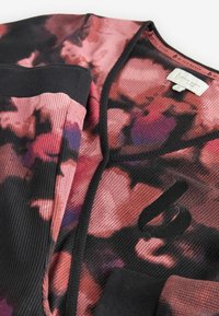 Patterned cardigan in shades of pink and black, featuring ribbed texture, v-neck, and small logo detail near the hem. Soft fabric.