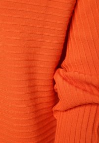 Oranger geriffelter Stoff mit texturierter Oberfläche, der subtile Streifen und eine glatte Oberfläche aufweist. Teile sind gerafft, was auf Drapierung hinweist.