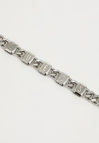 Silver chain bracelet featuring square links with the engraved letters "G," "U," "E," "S," and "S," interspersed with decorative accents.