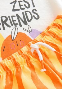 Cotton T-shirt with "ZEST FRIENDS" print and orange graphic, paired with orange and yellow striped elastic shorts featuring a white drawstring.